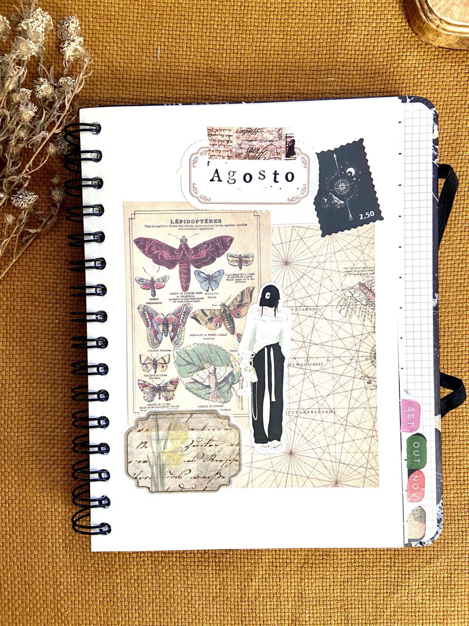 Uma folha branca de um scrapbook com adesivos colados. Em destaque, é possível ver um adesivo com a escrita: Agosto e outros com vários insetos que parecem borboletas.